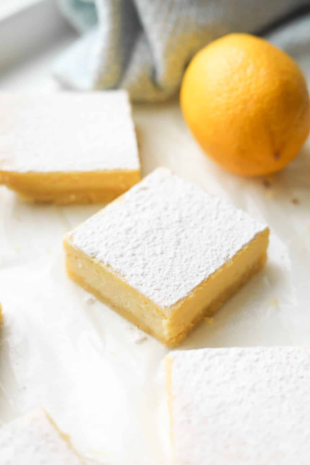 Lemon bars on parchment paper next to a lemon.