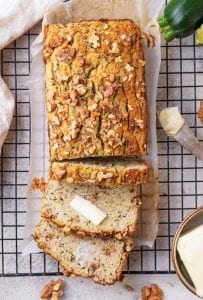 Zucchini bread with 3 slices cut from it and 2 of the slices covered with butter.