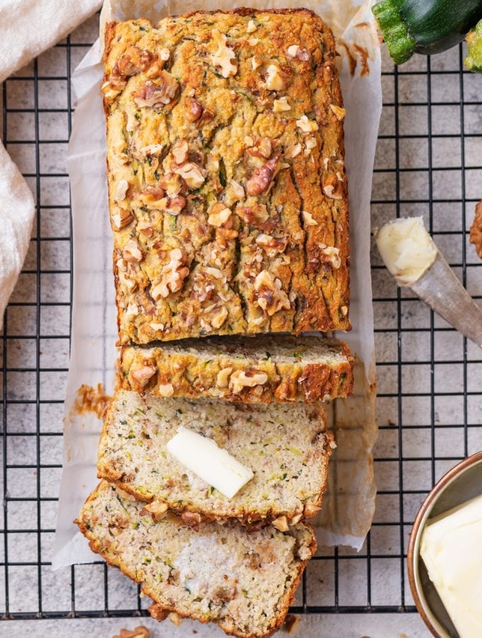 Zucchini bread with 3 slices cut from it and 2 of the slices covered with butter.