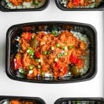 A meal prep container filled with cauliflower rice and topped with BBQ chicken and vegetables.