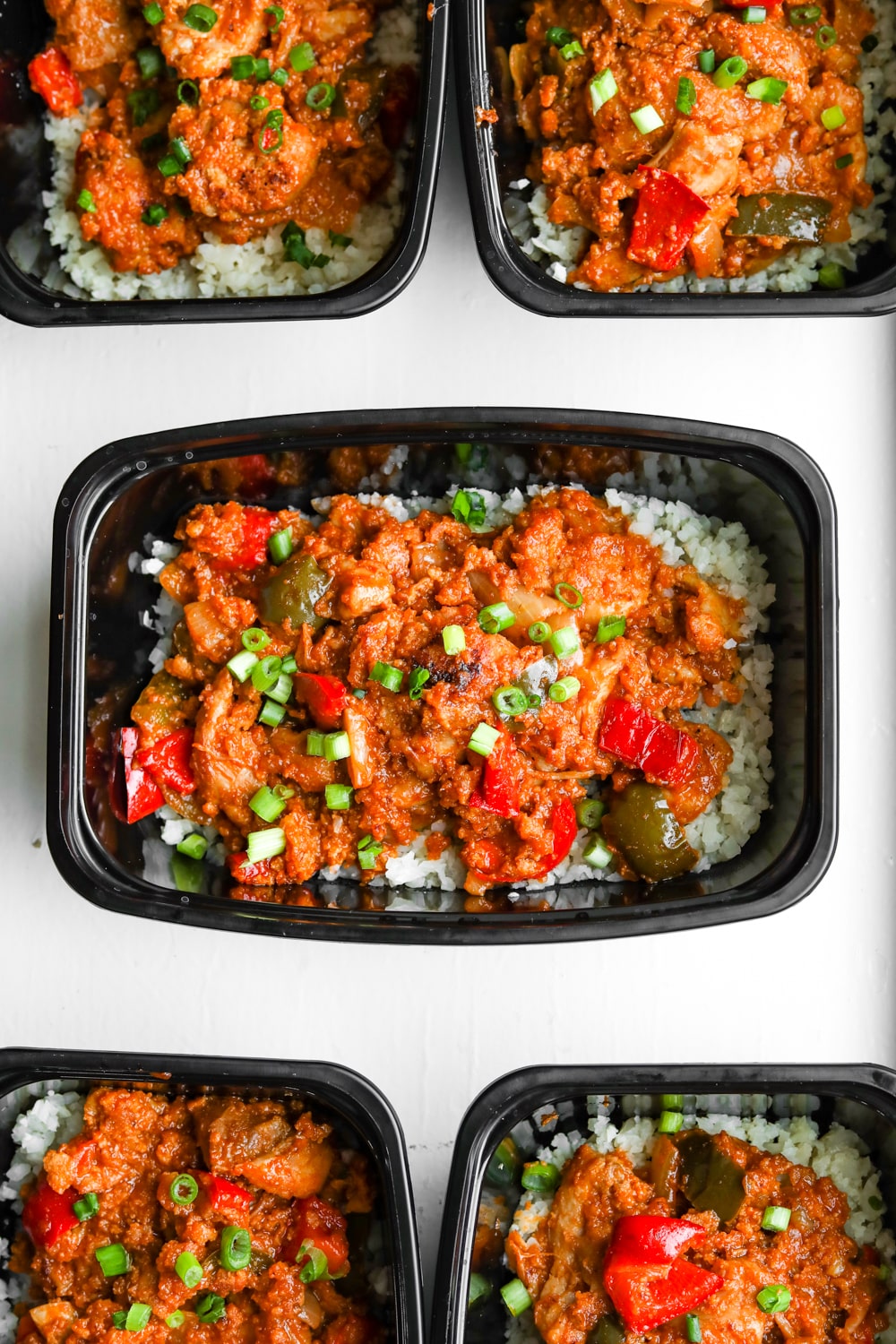 A meal prep container filled with cauliflower rice and topped with BBQ chicken and vegetables.