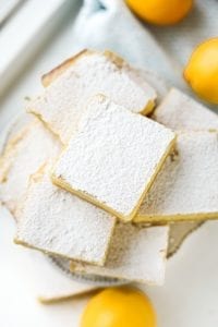 Keto lemon bars stacked on top of one another on a small cake plate.