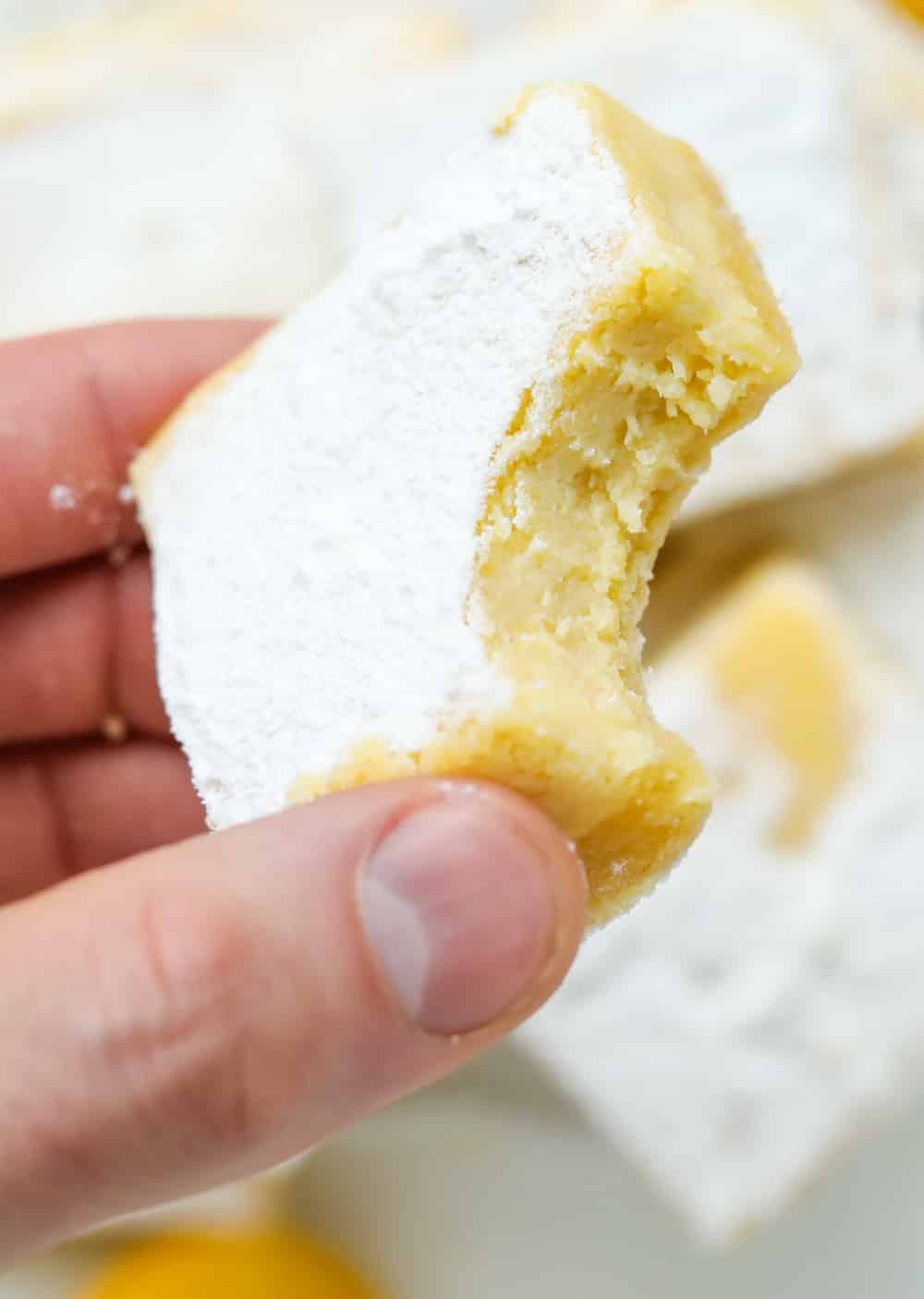 A hand holding a lemon bar that's been bitten into.