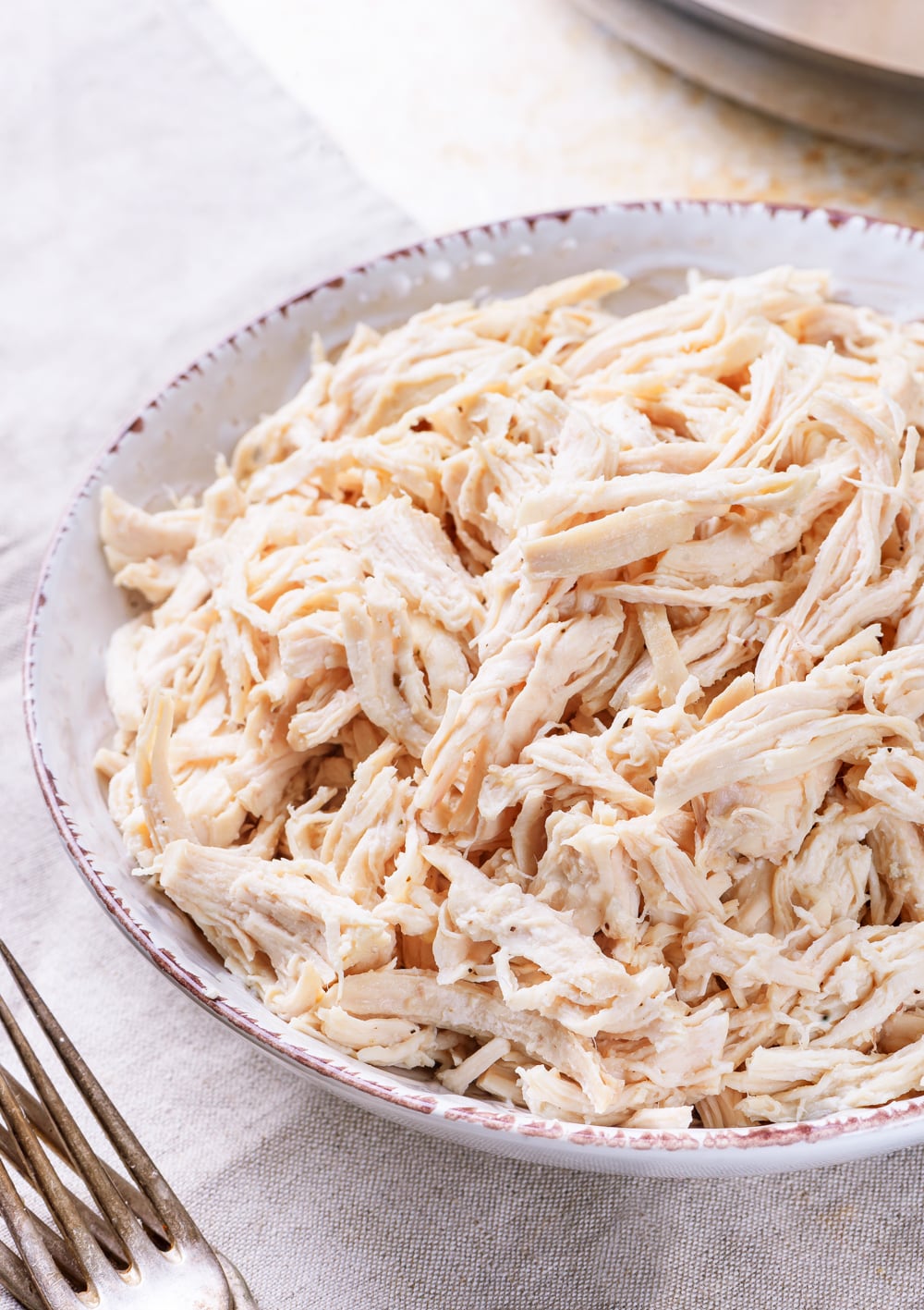 Chicken in a bowl next to a couple of forks.