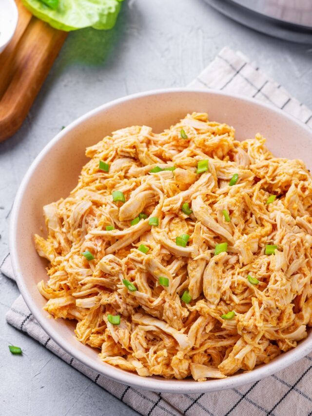 Shredded Buffalo chicken in a white bowl, and topped with green onions.