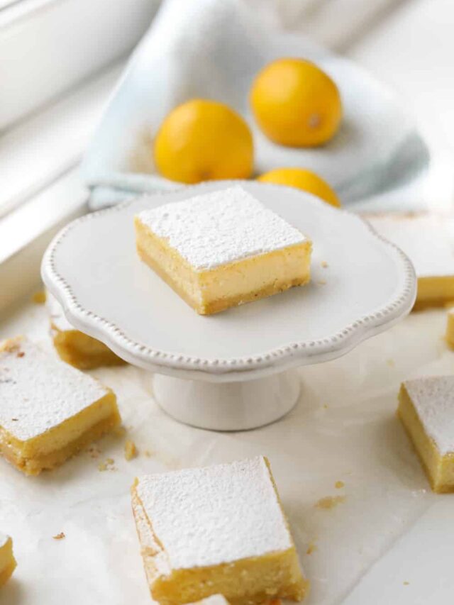 A keto lemon bar on a serving dish with lemons behind it.