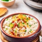 A bowl of crack chicken topped with green onions and bacon.