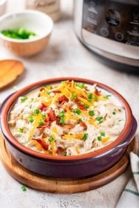 A bowl of crack chicken topped with green onions and bacon.