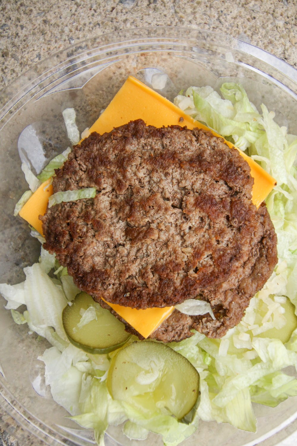 2 Beef patties with a slice of American cheese between them stacked on top of shredded lettuce, diced onions, and sliced pickles.