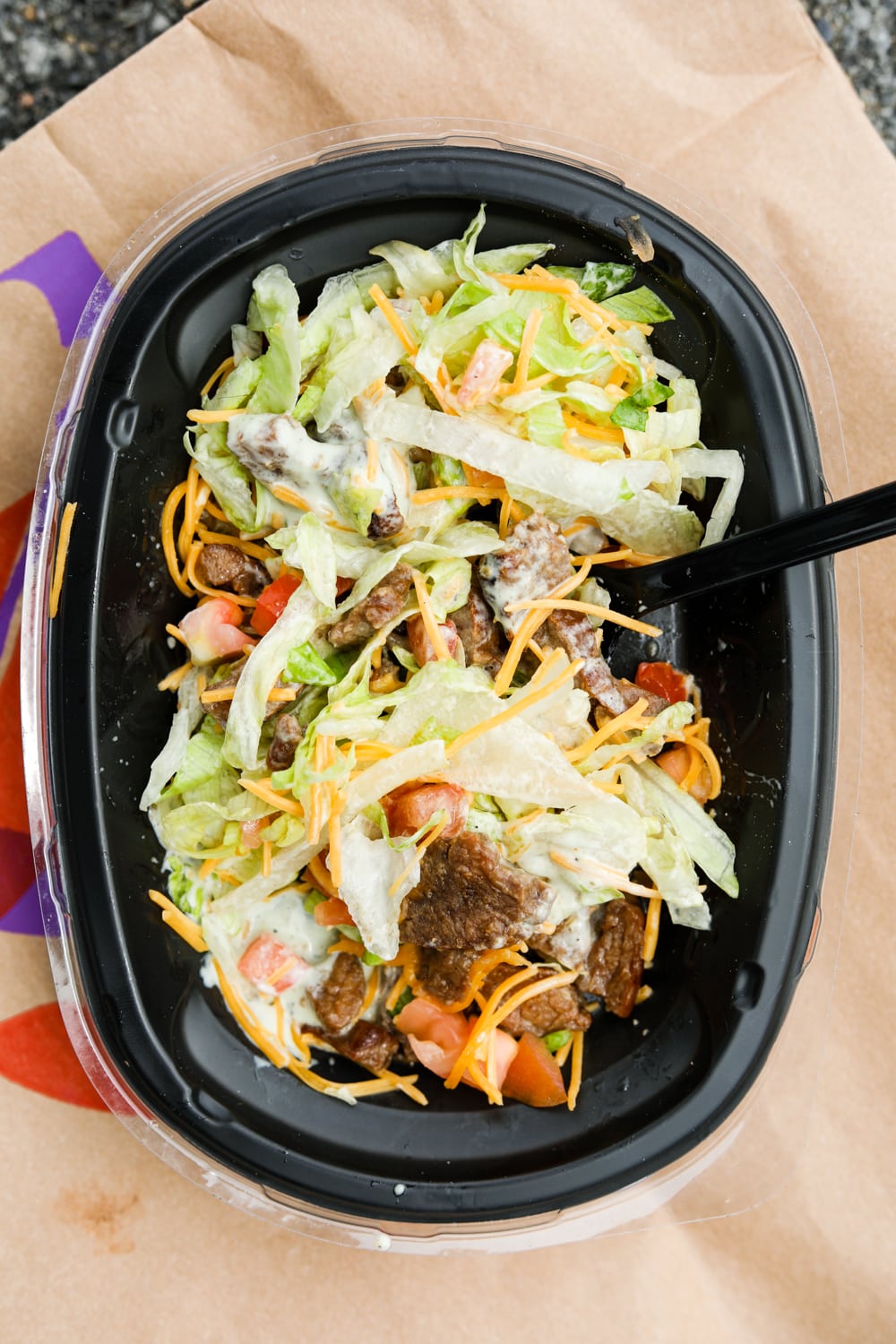 A bowl full of shredded lettuce, cheese, pico de gallo, and thin strips of steak.