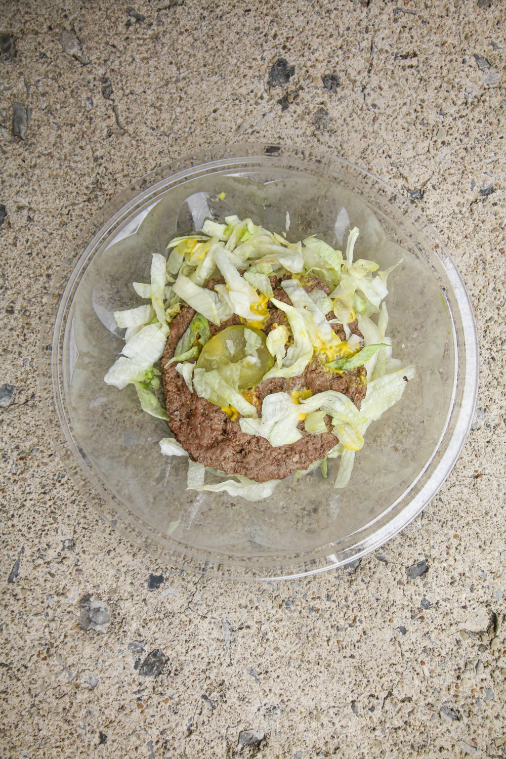 A hamburger on top of a bed of shredded lettuce and topped with pickle slices and mustard.