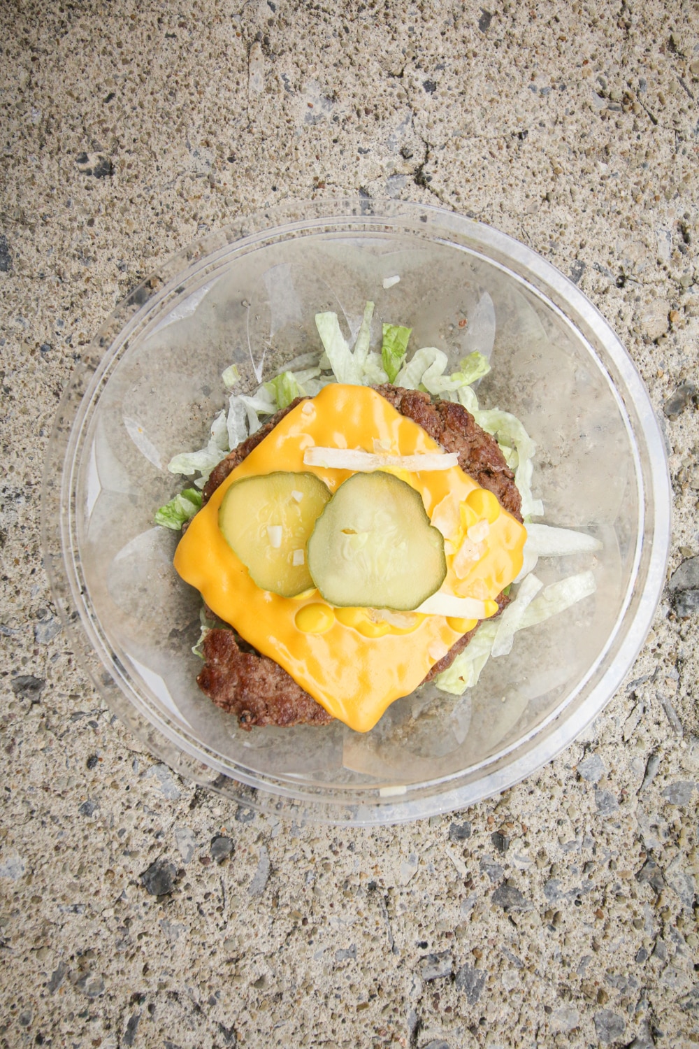 A ¼ pound beef patty on top of shredded lettuce and topped with cheese, sliced pickles, onions, and mustard.