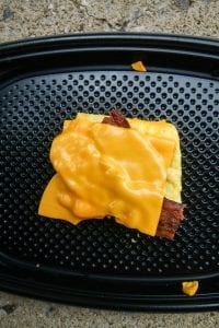 2 Slices of bacon on top of a folded egg and topped with American cheese.