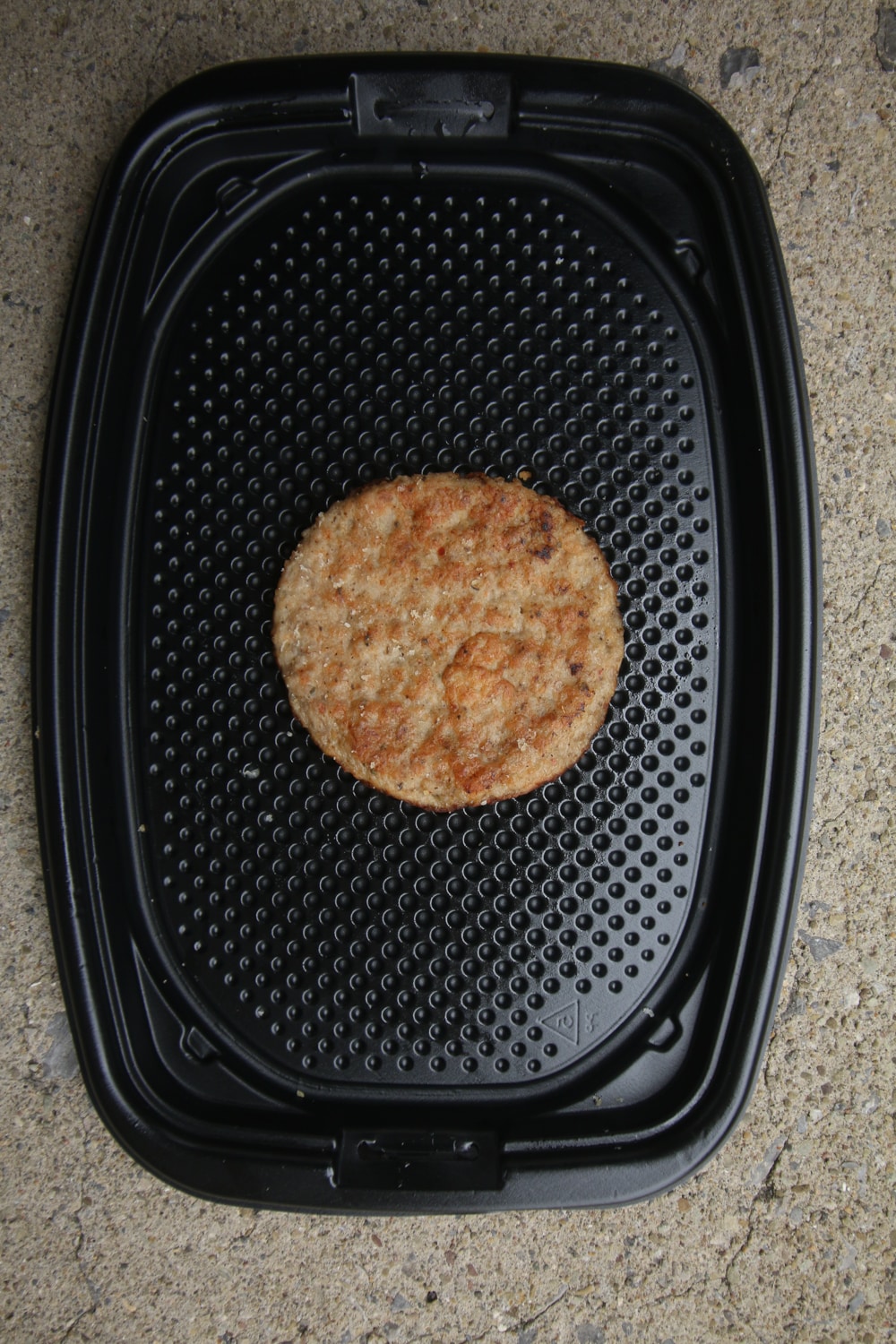 A breakfast sausage patty on a black take-out container.