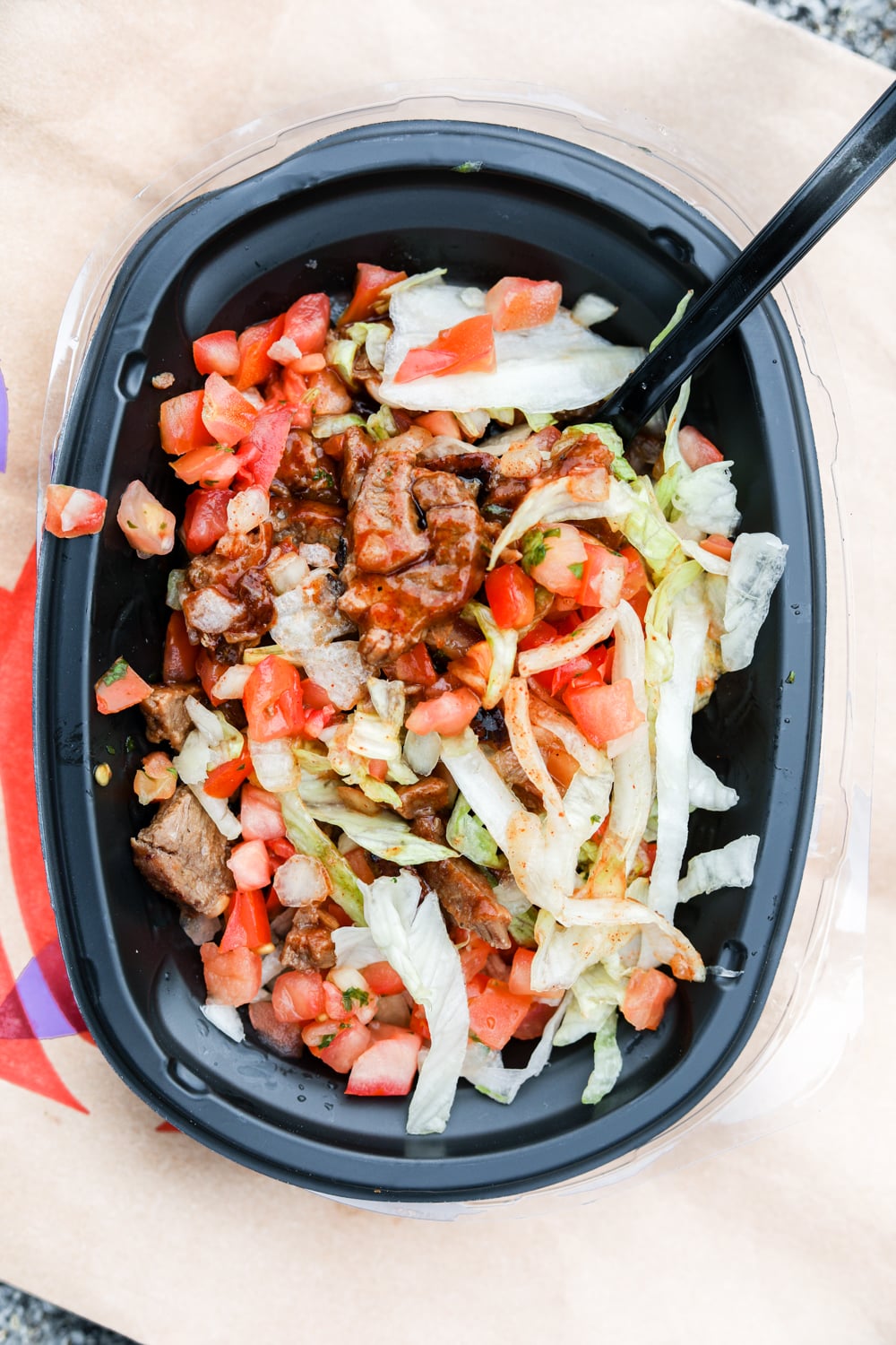 Shredded lettuce, pico de gallo, and chopped steak, topped with hot sauce in a black bowl.