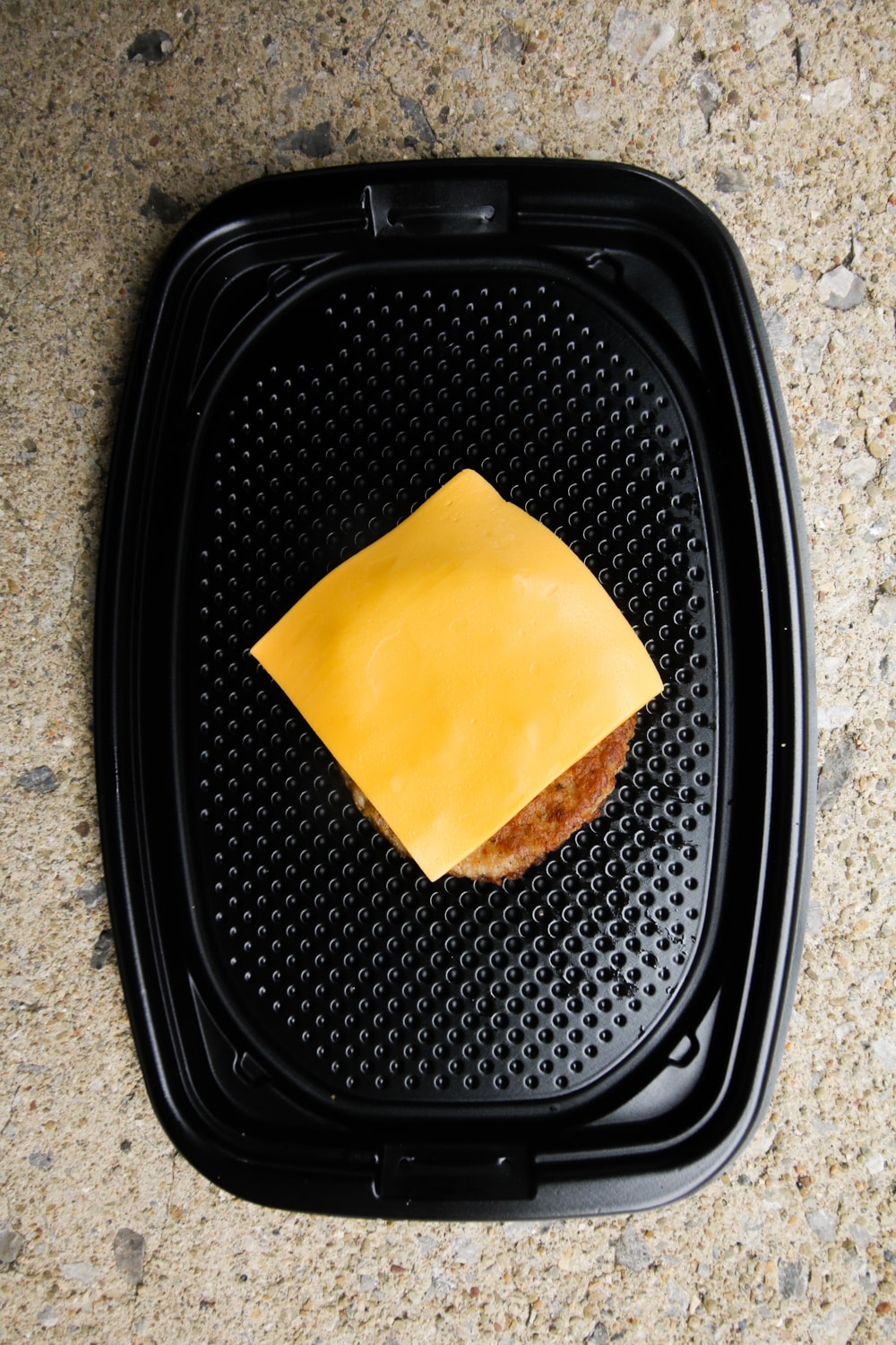 A piece of sausage topped with cheese on a black take-out container.