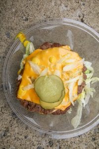 Two ¼ pound beef patties in a bowl of shredded lettuce and topped with cheese, diced onions, pickles, and mustard.