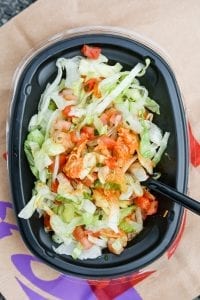 A bowl full of shredded lettuce, pico de gallo, shredded cheese, and sliced chicken.