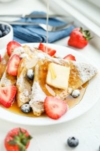 A plate of French toast with syrup being poured on it.