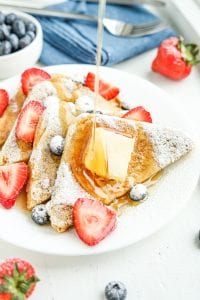 French toast on a white plate with syrup being poured on the toast.