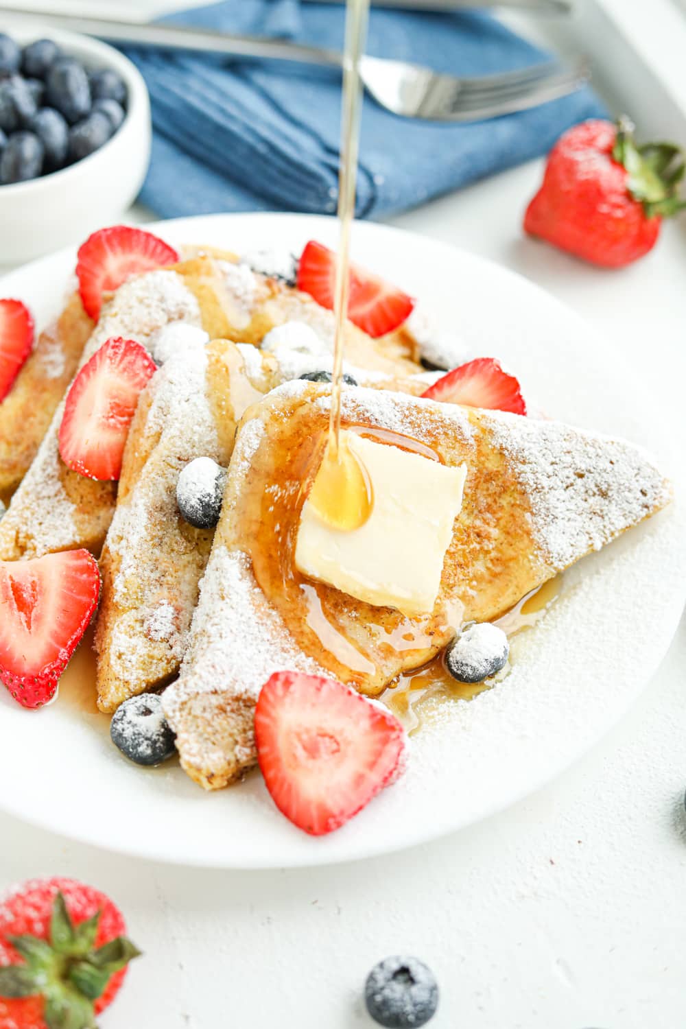 4 Slices of French toast on a white plate with syrup being poured on the toast.