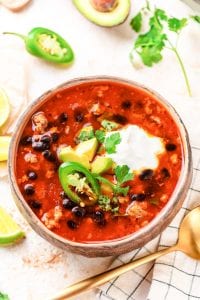 A bowl of taco soup topped with sour cream, avocado, and jalapeños.