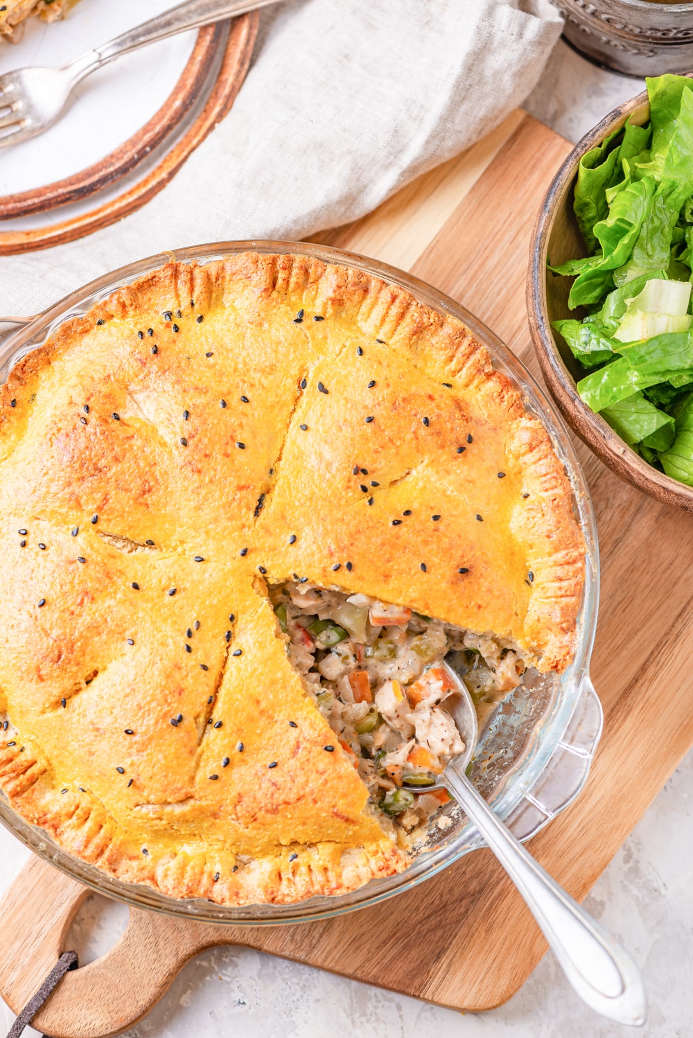 A pie plate board filled with chicken pot pie on top of a cutting and next to a bowl of lettuce.