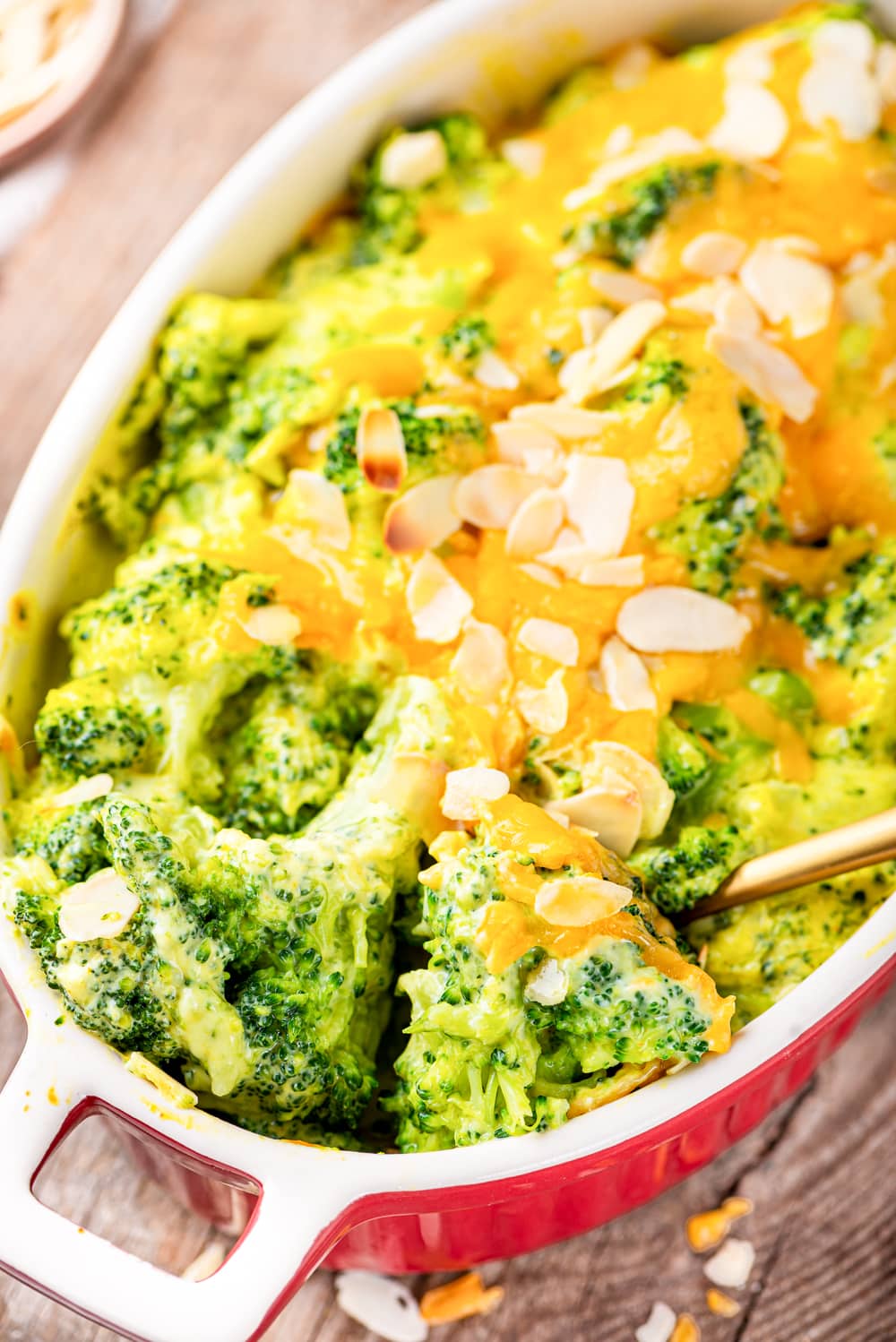 Broccoli florets covered in cheese about to be served from a casserole dish with a golden spoon.