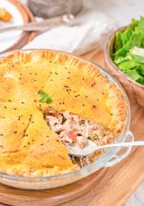 An entire chicken pot pie with a slice of crust removed, and a spoon is wedged into the filling.