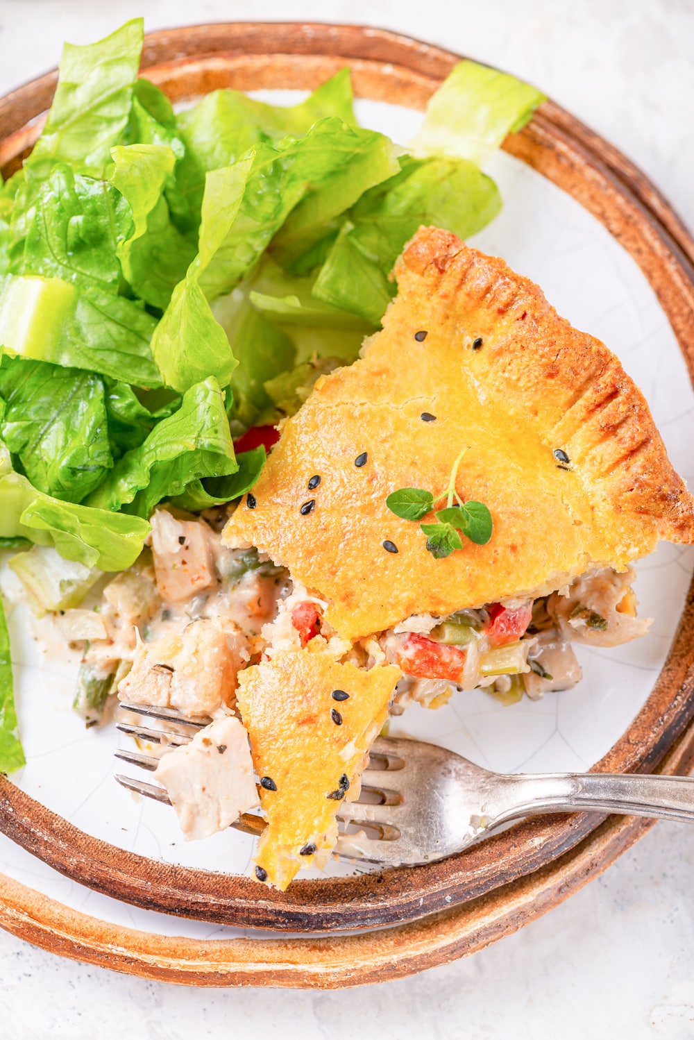 A slice of chicken pot pie on a plate with a salad next to it.