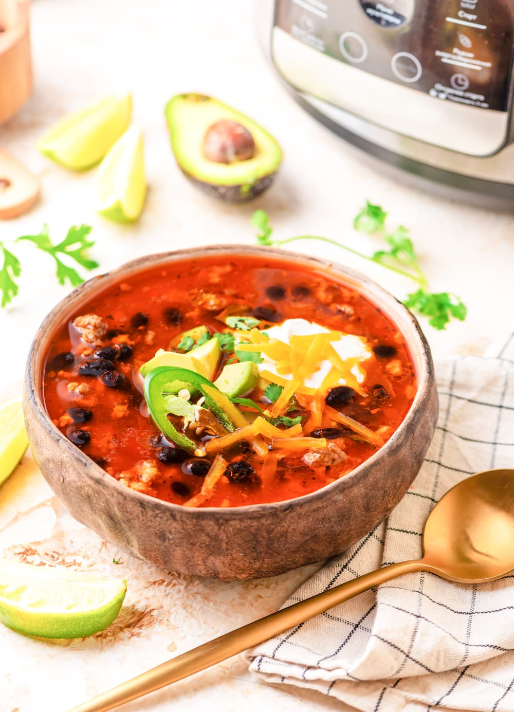 A bowl of soup next to a gold fork, a napkin, and a cut open avocado.