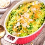 A casserole dish filled with broccoli and cheese on a wooden cutting board.