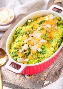 A casserole dish filled with broccoli and cheese on a wooden cutting board.