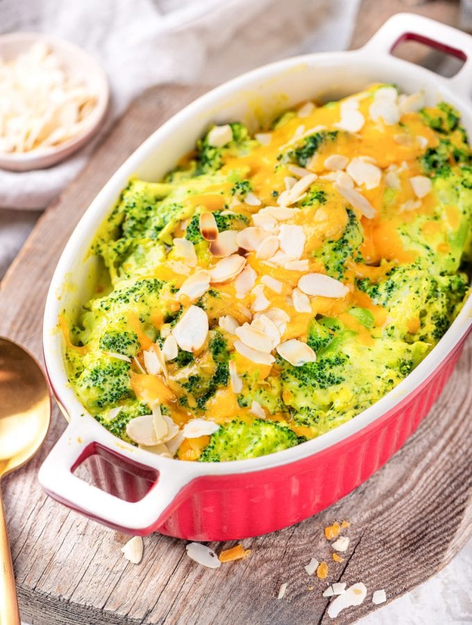 A casserole dish filled with broccoli and cheese on a wooden cutting board.