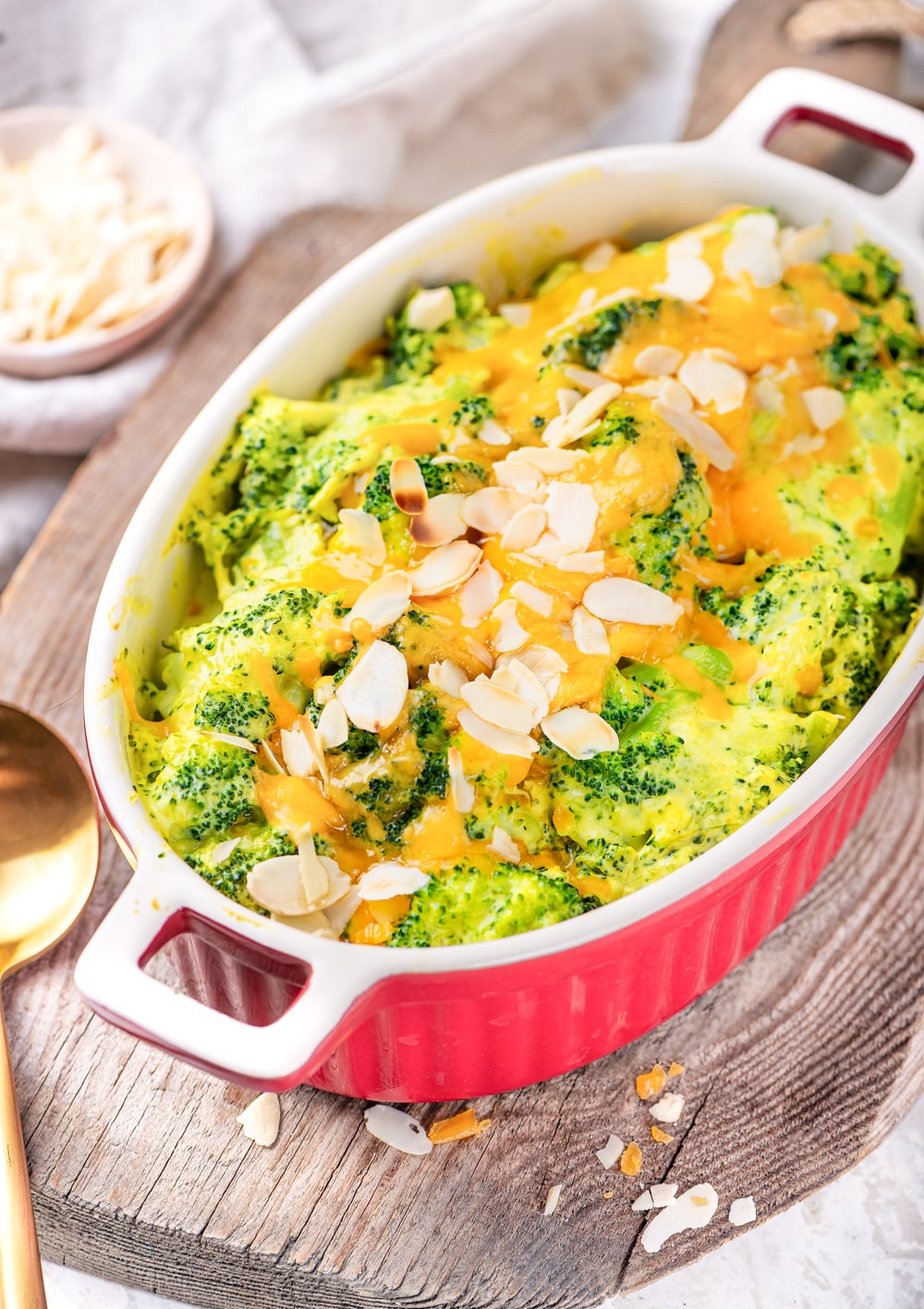 A casserole dish filled with broccoli and cheese on a wooden cutting board.