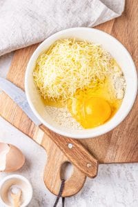 A white bowl filled with almond flour, coconut flour, butter, cheese, and an egg.