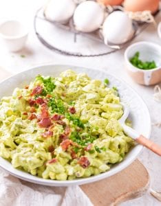 A bowl filled with egg salad that's topped with bacon and chives.