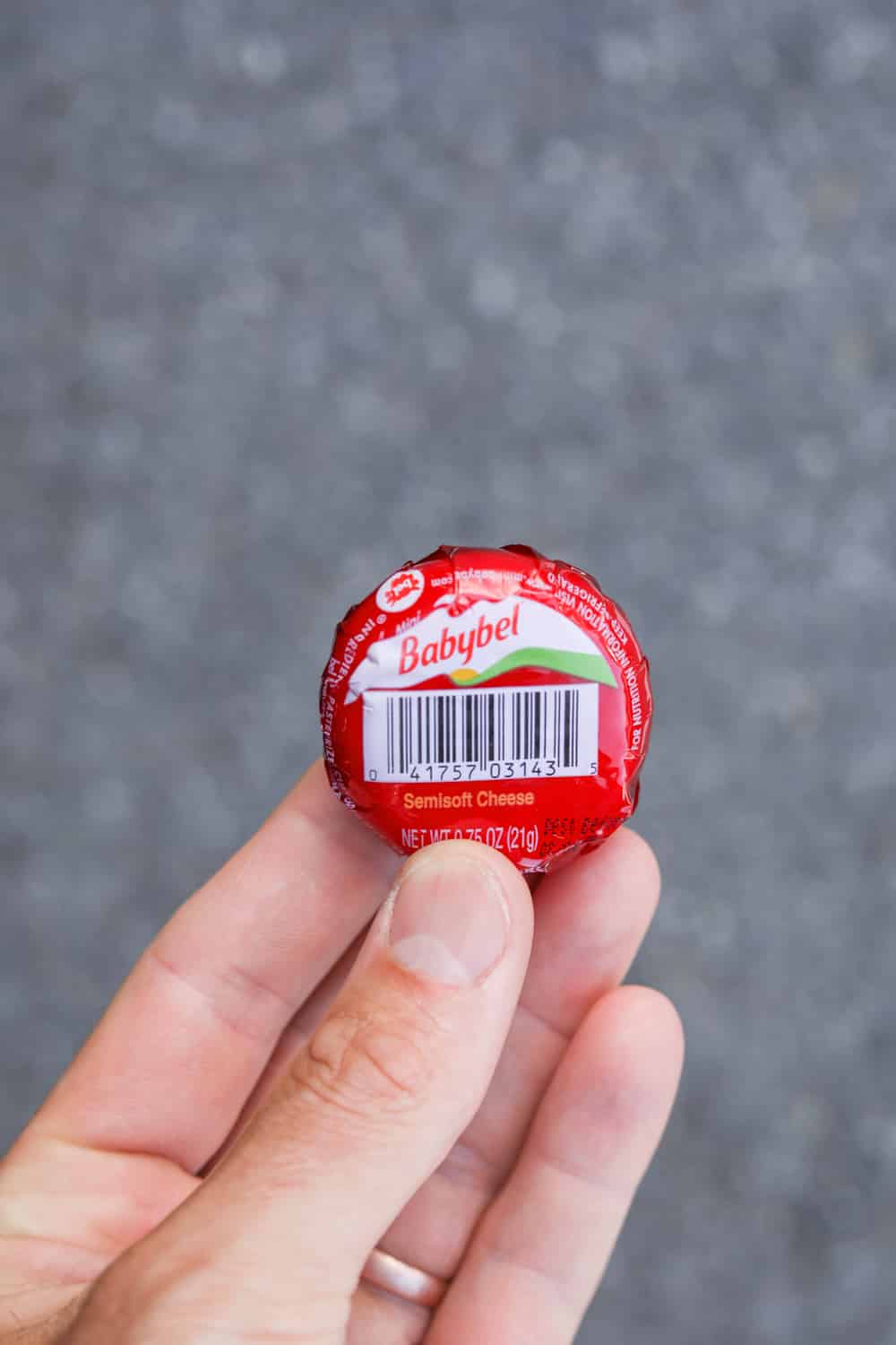 A hand hold an individually wrapped cheese wheel.