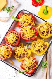 8 bell peppers halves stuffed with ground beef and topped with unmelted cheddar cheese on a baking sheet.