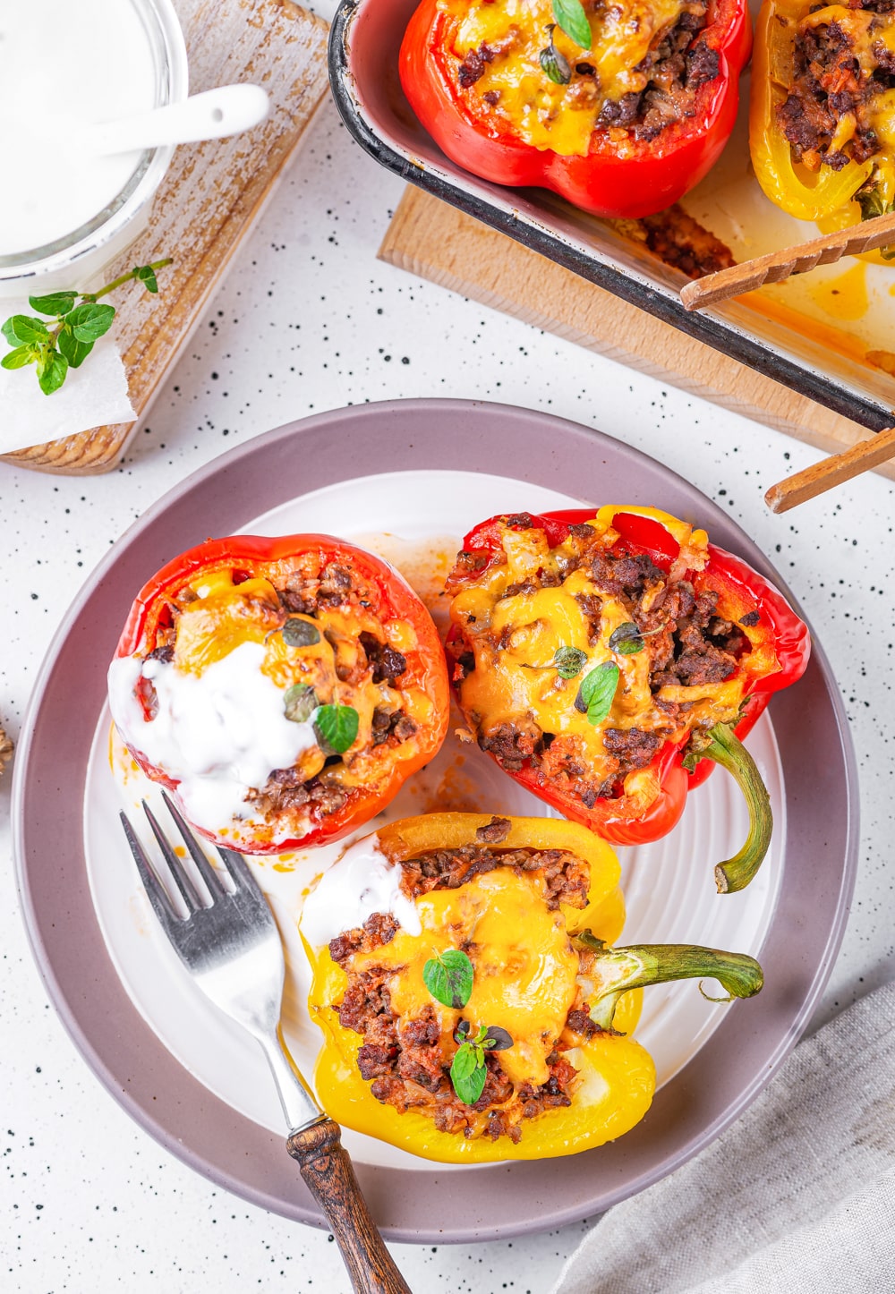 3 Bell peppers on a plate that have been cut in half and stuffed with ground beef, cauliflower rice, and cheese.