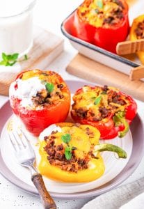 A plate filled with multiple stuffed bell peppers & one of them is topped with sour cream.