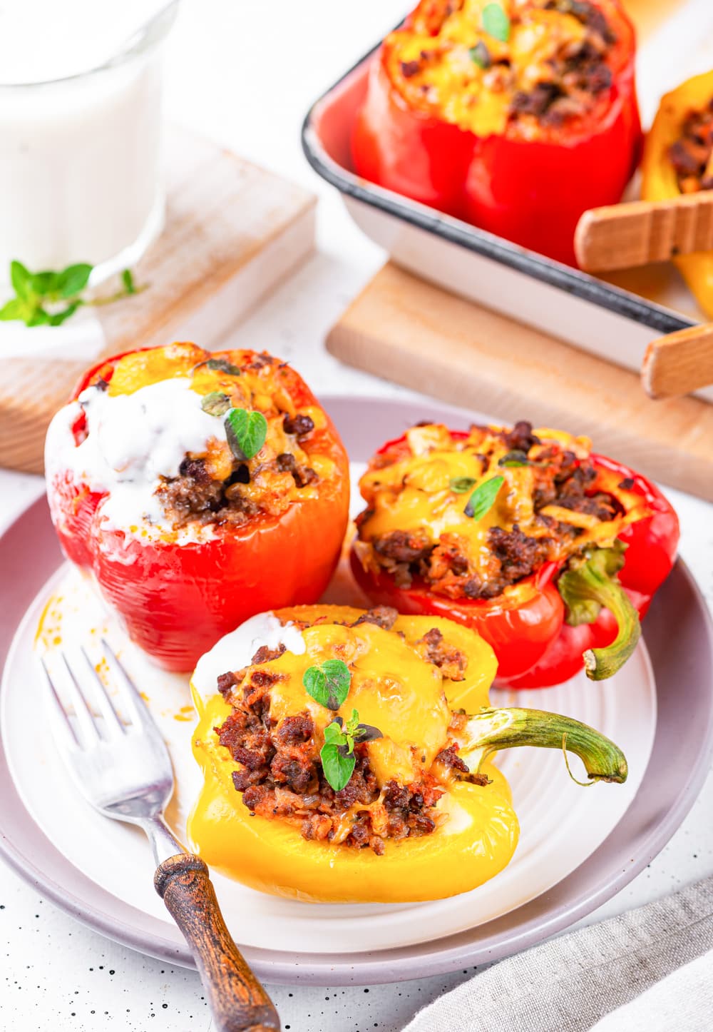 A plate filled with multiple stuffed bell peppers & one of them is topped with sour cream.