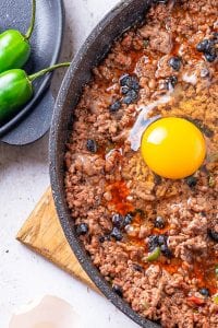 An egg in a skillet filled with ground beef and black soybeans.