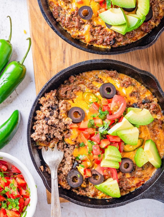 A fork taking a serving of ground beef and cheese out of a cast iron skillet.