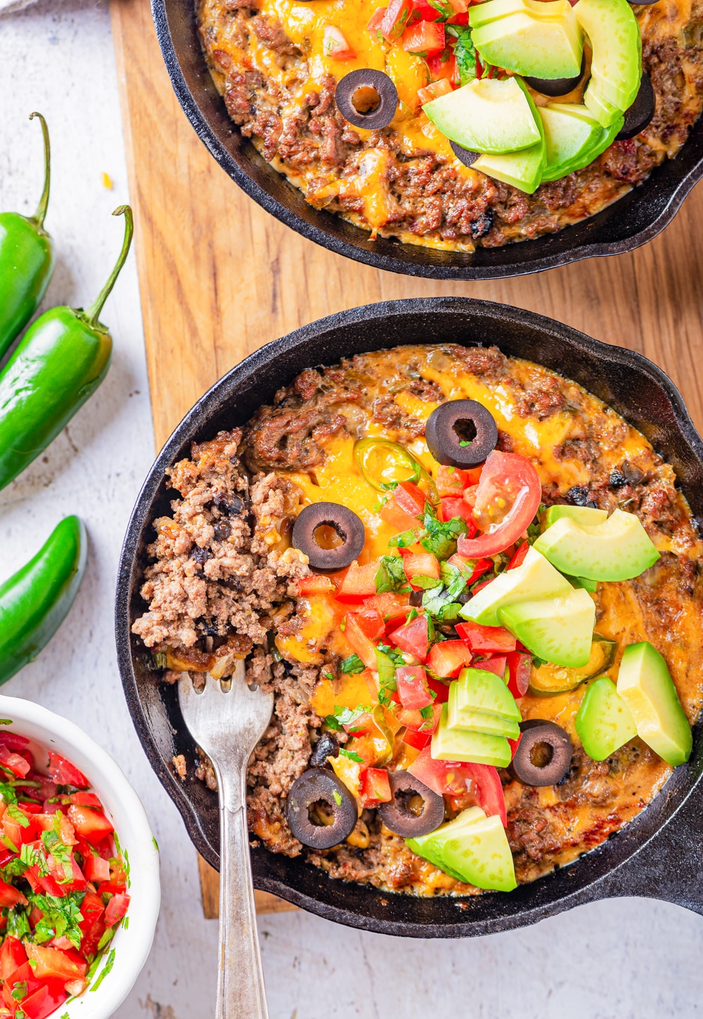 A fork taking a serving of ground beef and cheese out of a cast iron skillet.