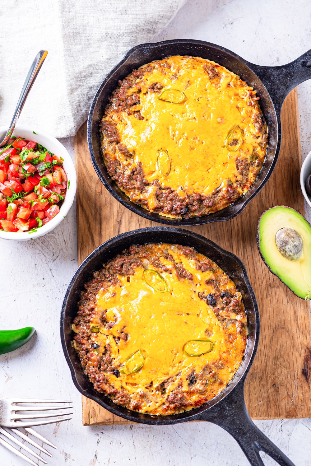 2 skillets filled with ground beef and topped with melted cheese.