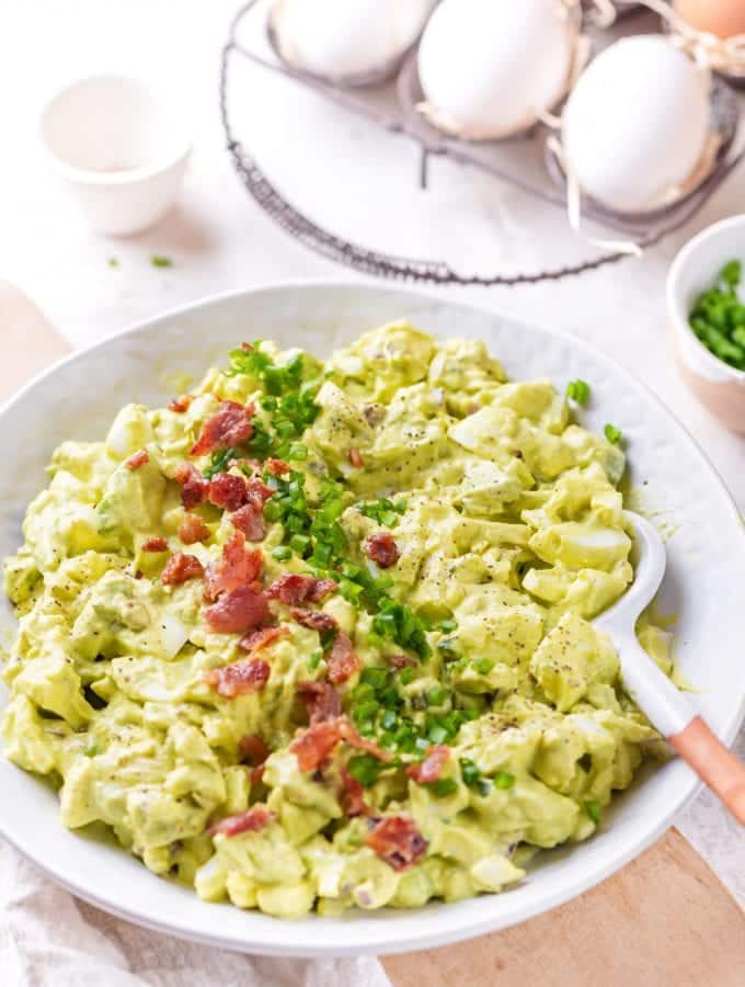 Egg salad in a white bowl topped with bacon and chives.