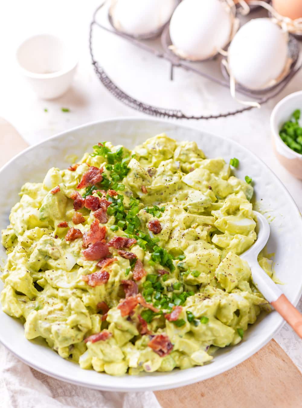 Egg salad in a white bowl topped with bacon and chives.