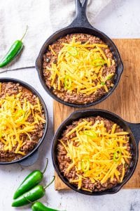 3 Black cast-iron skillets filled with cooked ground beef, and topped with shredded cheddar cheese.