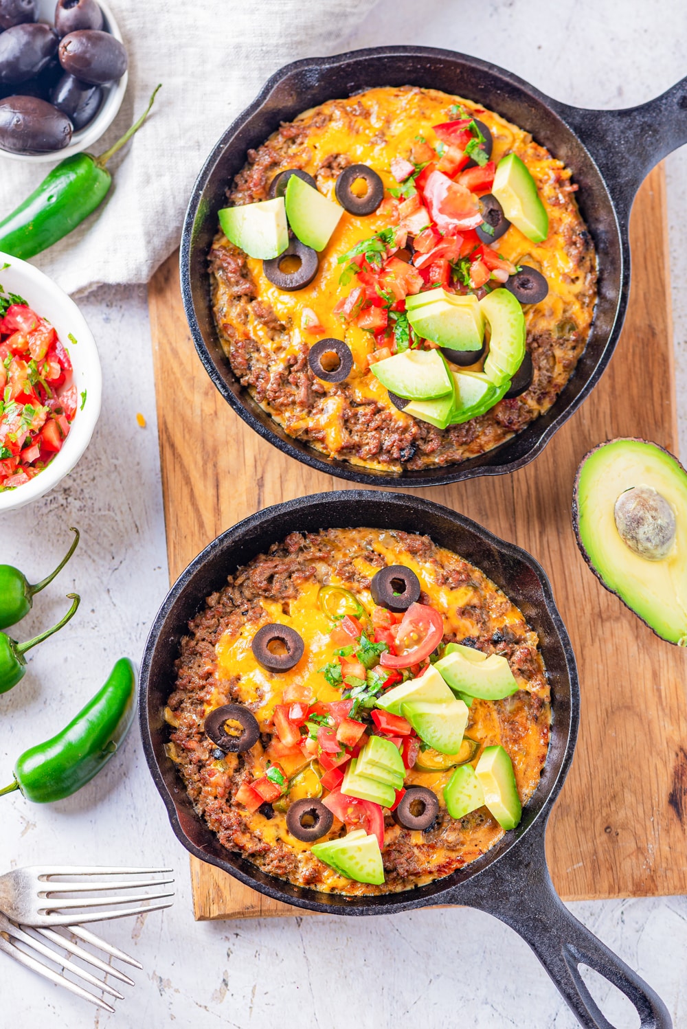 2 Cast iron skillets filled with ground beef, cheese, salsa, and pieces of avocado.